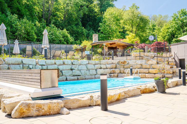 Pool im Außenbereich der Saunawelt umzäunt von Natursteinmauern.