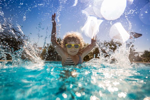 Kind mit Sonnebrille planscht im Wasserbecken und blickt in die Kamera