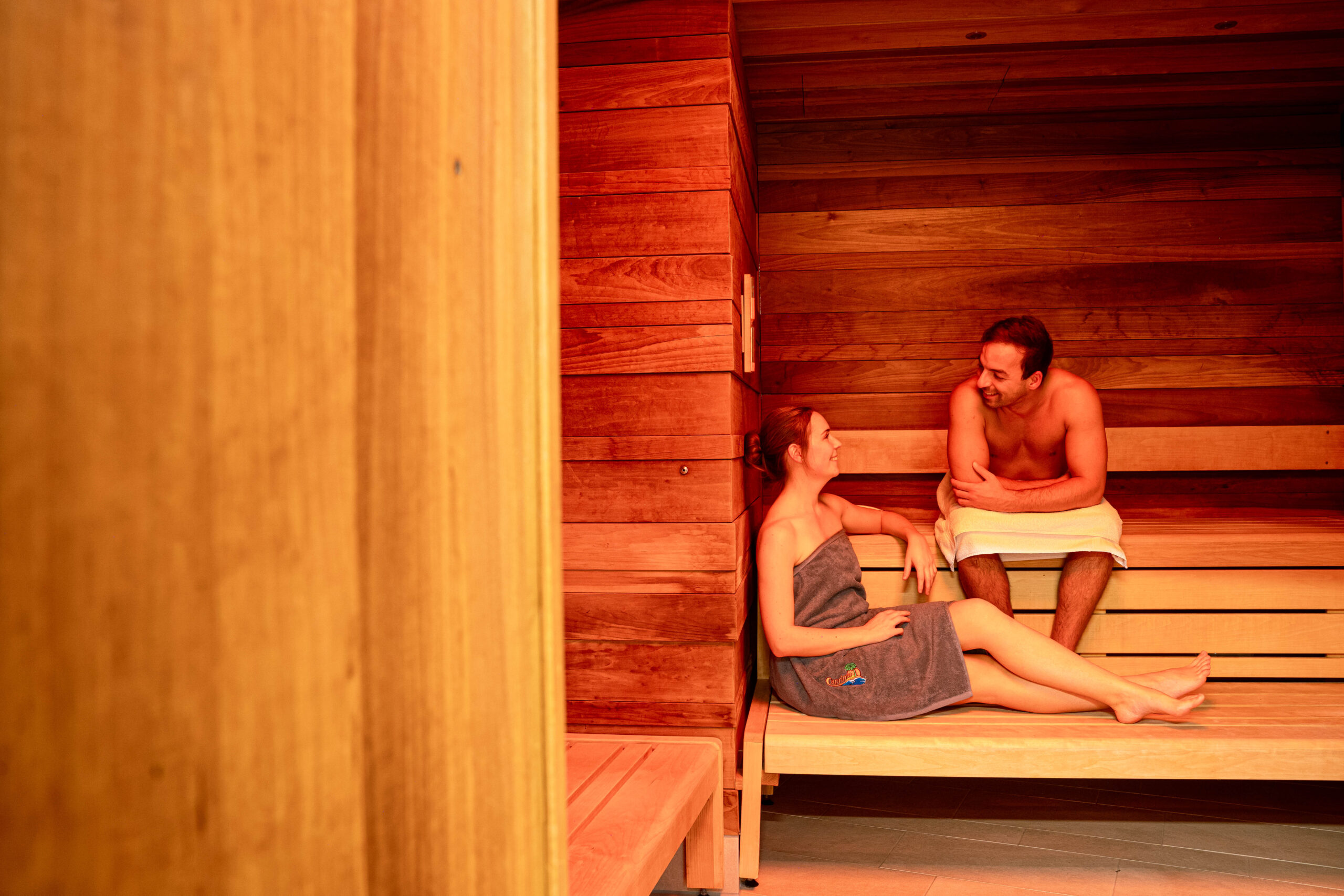 Ein Mann und eine Frau sitzen entspannt in einer Sauna mit gemütlicher warmer Beleuchtung.