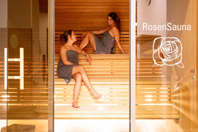 Zwei Frauen unterhalten sich entspannt in der stilvollen "RosenSauna" mit heller Holzverkleidung.